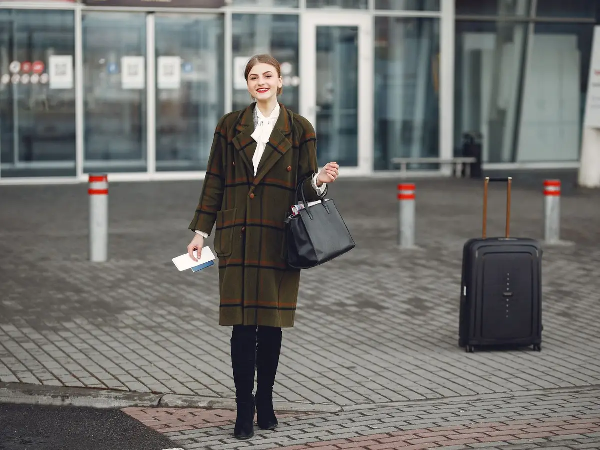 A traveler with a suitcase at an airport pick-up curb