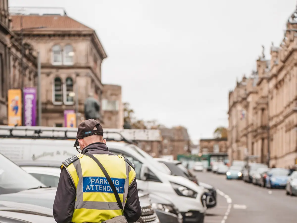 A parking attendant in a high-visibility vest on a city street