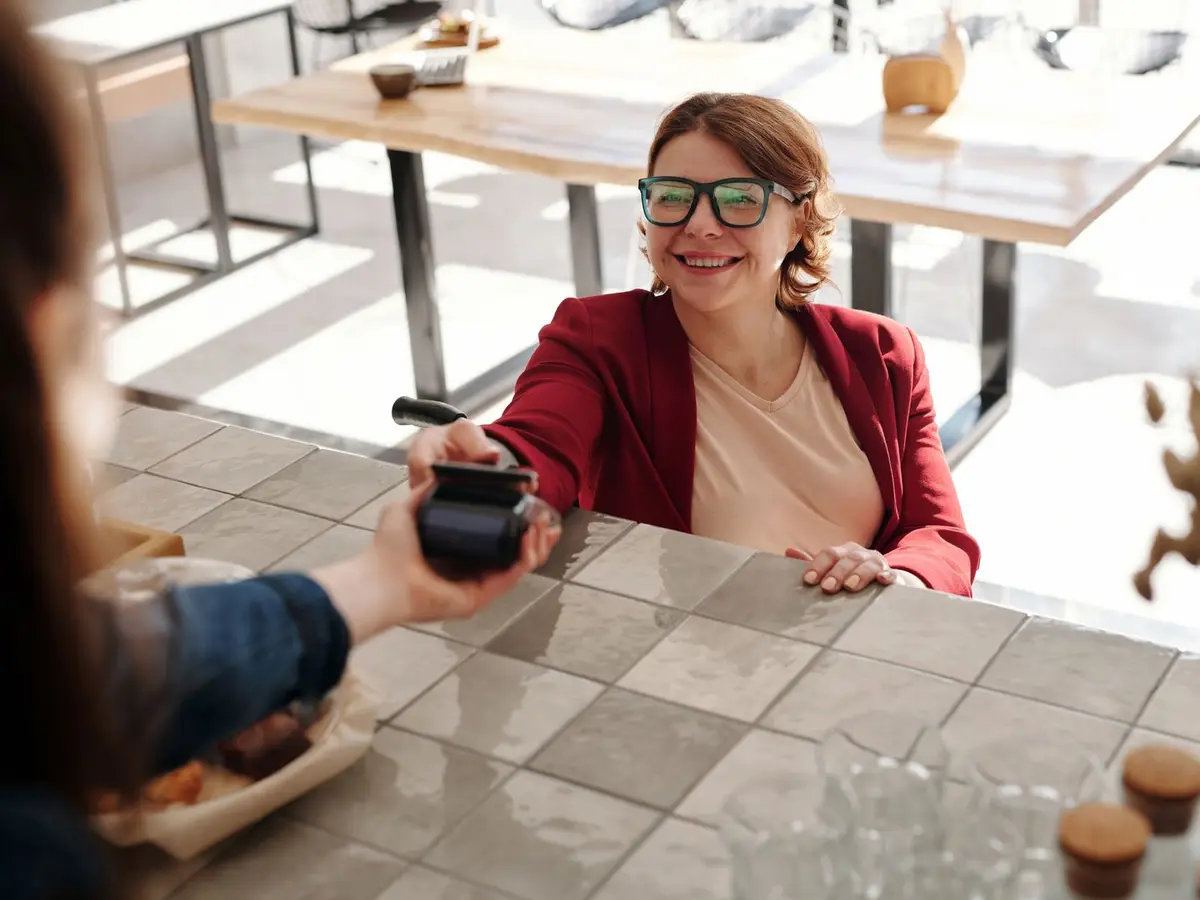 A smiling woman paying with her phone at a café table