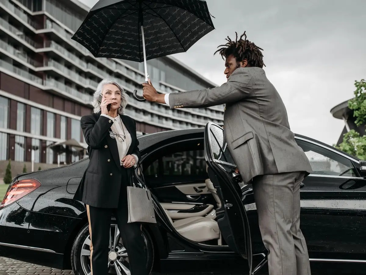 A man holding an umbrella and opening a car door for a woman outside a hotel